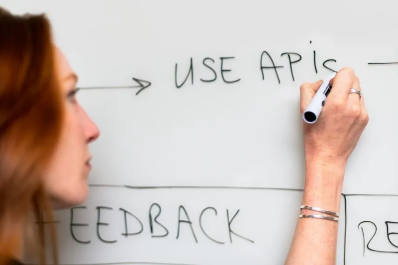 A woman writing 'use APIs' on a whiteboard