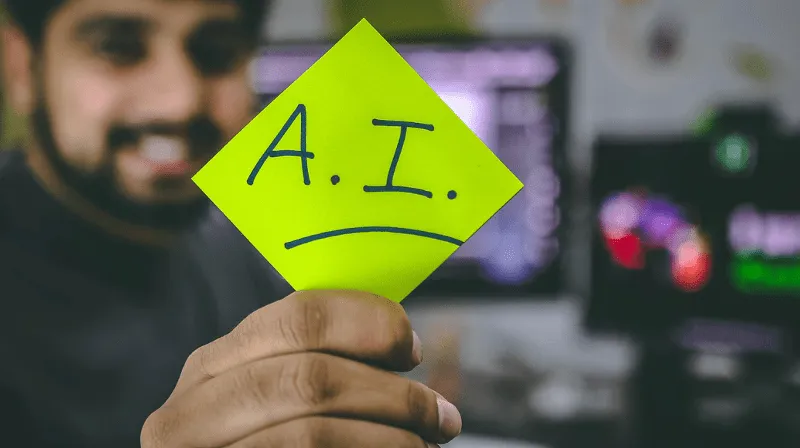 Image of a person holding a sticky note that has AI written on it