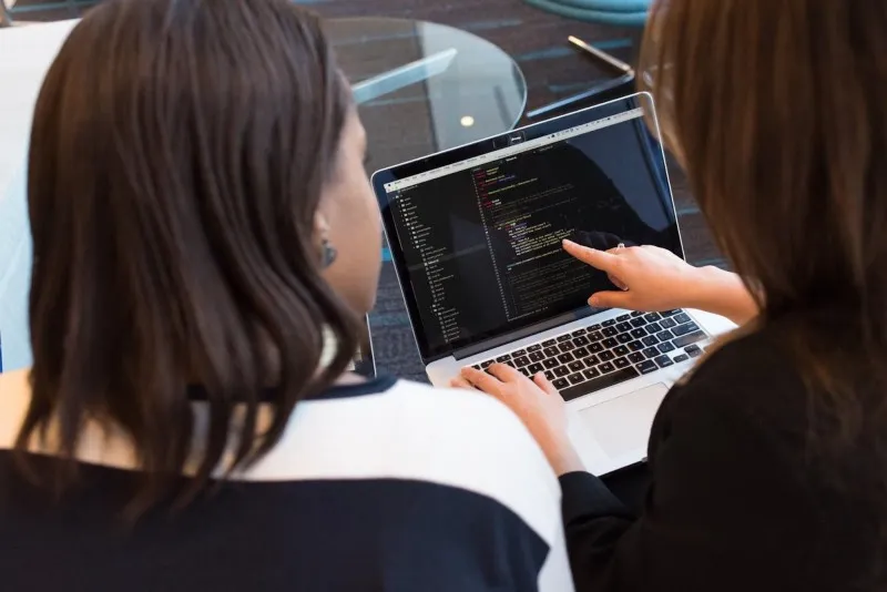 Two people looking at code on a laptop screen