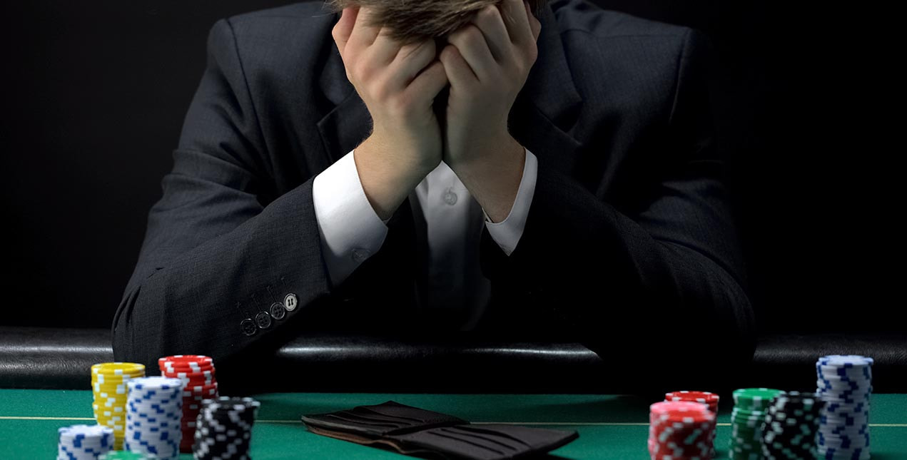 A man with his head in his hands and his empty wallet at a casino table.